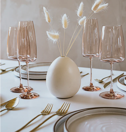 Стол, с гармонично лежащими обеденными столовыми приборами, 4 бокала и ваза оформленная в необычном стиле в ввиде яйца